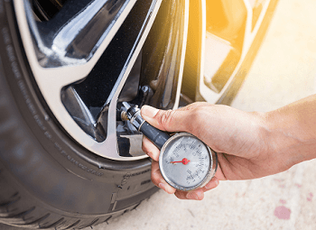 a hand using a pressure gauge to check on car tire