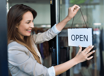 Woman small business owner puts an open sign on the door of storefront