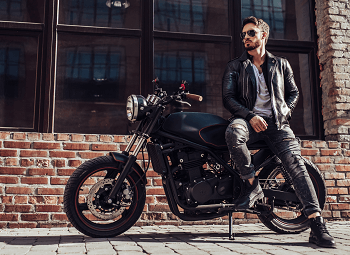 Man leaning against his motorcycle parked in front of a brick building